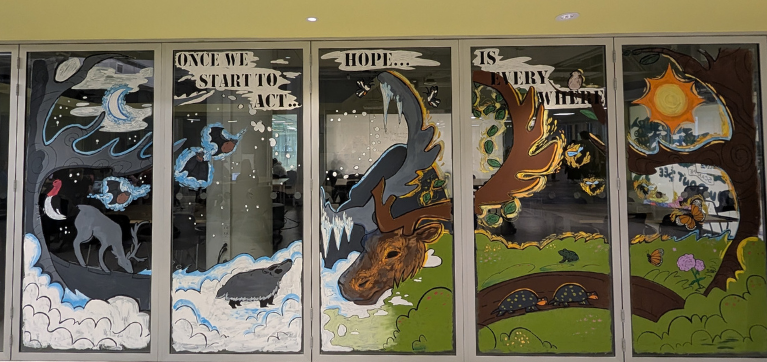 A multi-panel mural shows art painted on glass windows depicting elements of nature such as animals and trees, with the words 'once we start to act, hope... is everywhere'.
