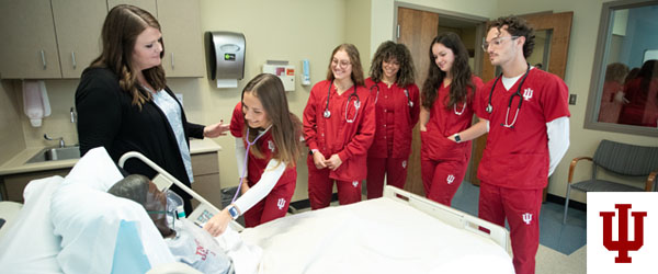 Five women and a man tend to a virtual patient in a hospital bed